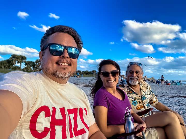 Maria's dad John sits on the beach with Maria and Neil while they wear their Chizu shirts in Englewood Beach, FL, US